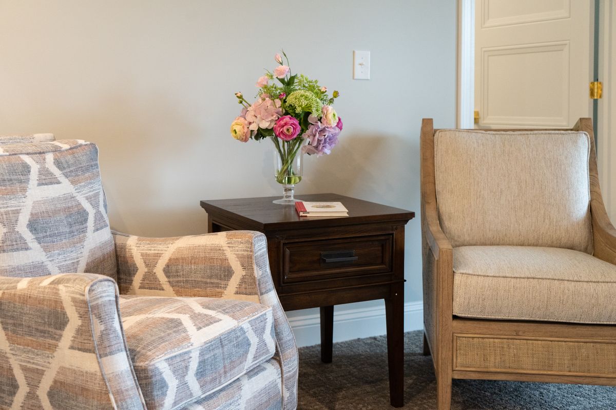 A cozy living room corner with a side table adorned with a vase of colorful flowers, flanked by comfortable armchairs.