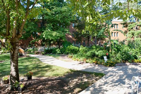 A serene garden pathway surrounded by lush greenery and a brick building in the background.