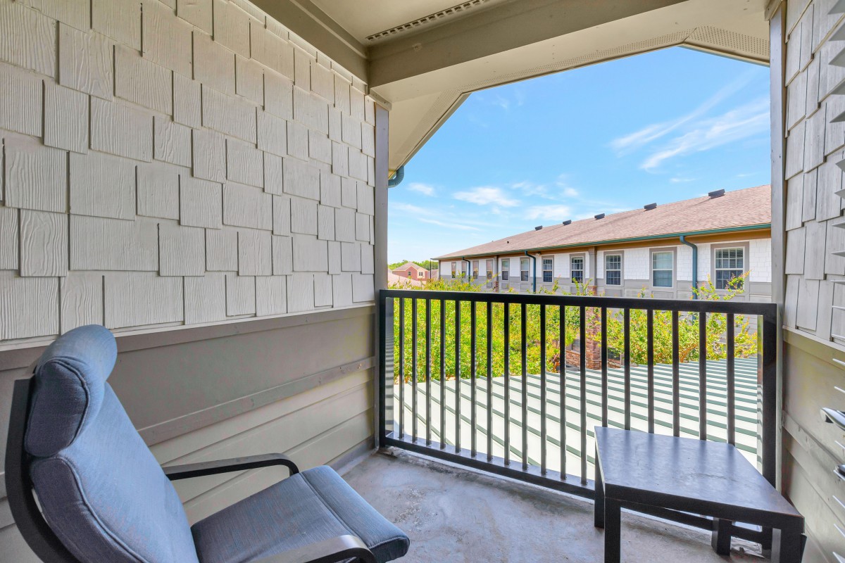 A cozy apartment balcony with chairs, offering a pleasant view of the surroundings under a clear blue sky.