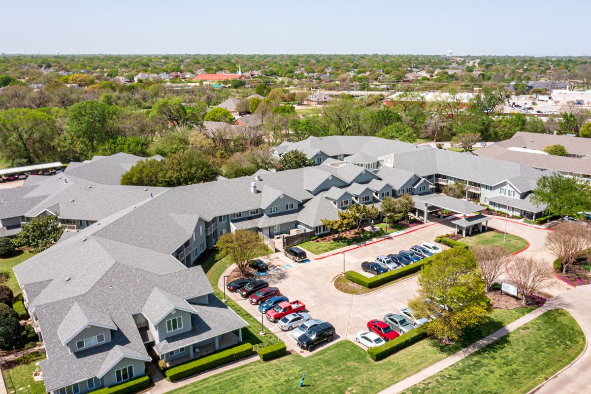 Aerial view of a residential building complex with a parking lot and surrounding greenery.
