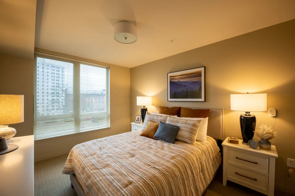 A modern and cozy bedroom with warm lighting and a large window.