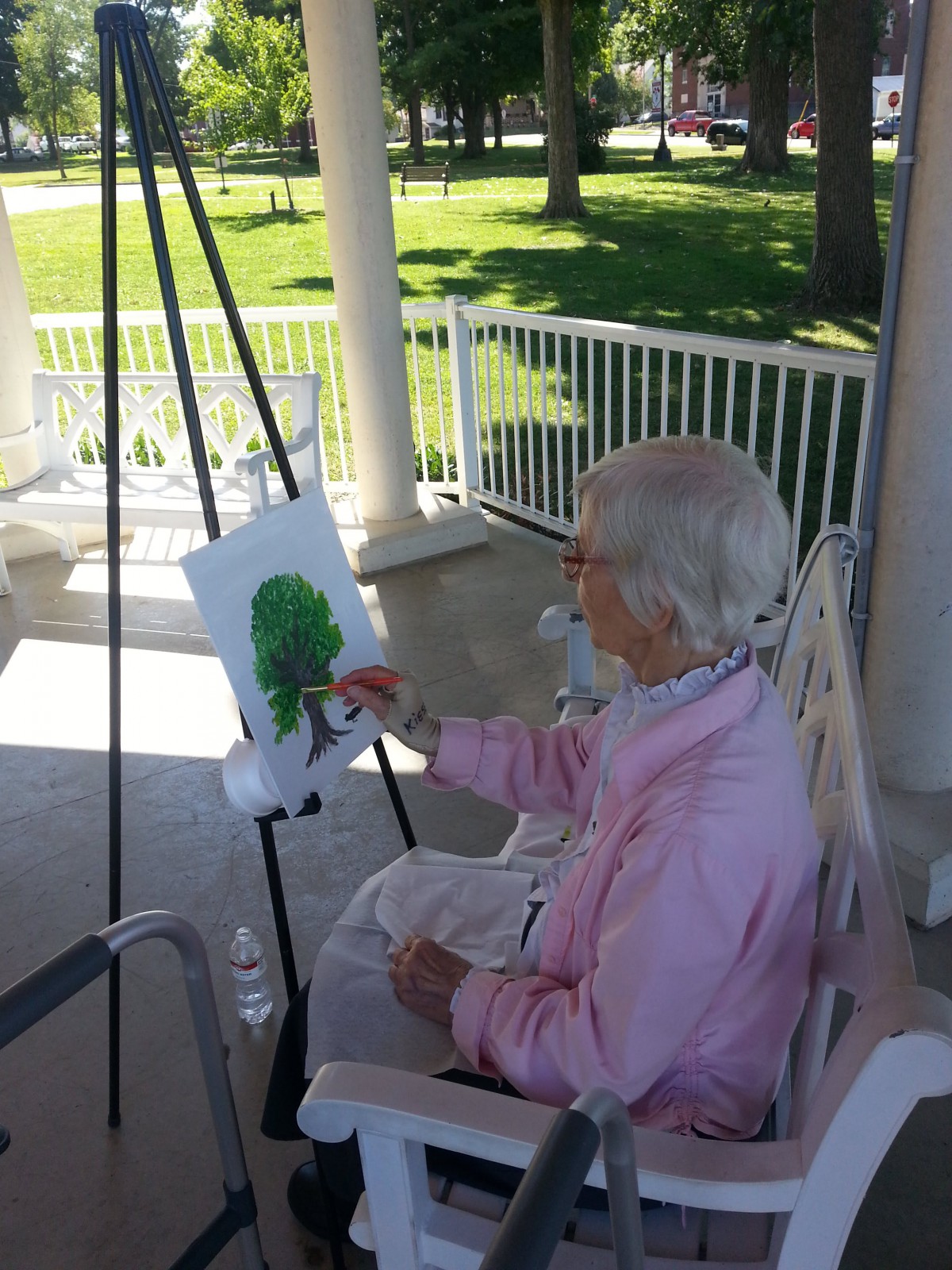 An elderly person painting outdoors on a sunny day.