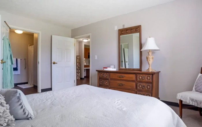 A cozy bedroom with a wooden dresser, mirror, and a table lamp.