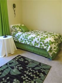 A bedroom with a green and white floral bedspread, matching curtains, and a decorative rug.