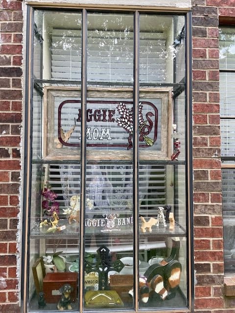 A window display with plants and a decorative sign against a brick wall.