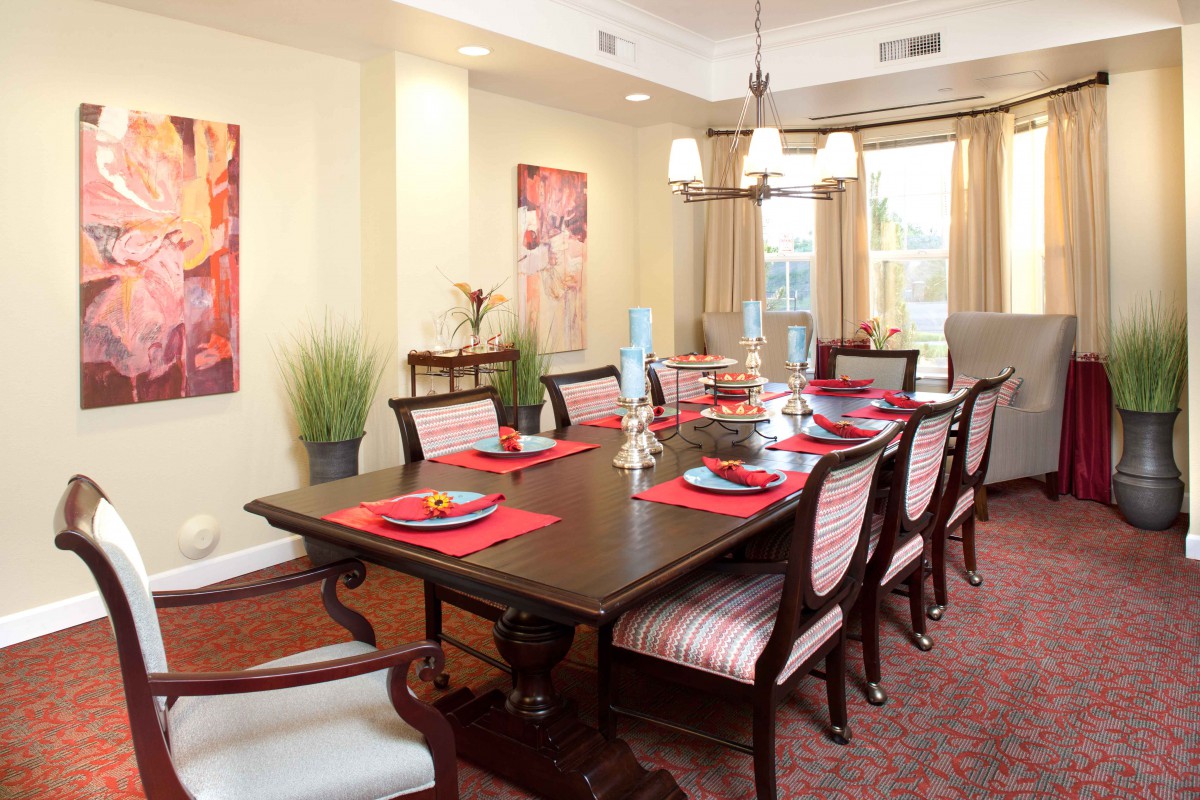An elegant dining room with a large table set for a meal, surrounded by chairs and illuminated by a chandelier.