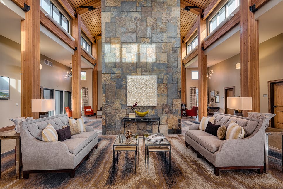 A luxurious, modern living room featuring high ceilings and a central stone wall with elegant furniture and wood beams.