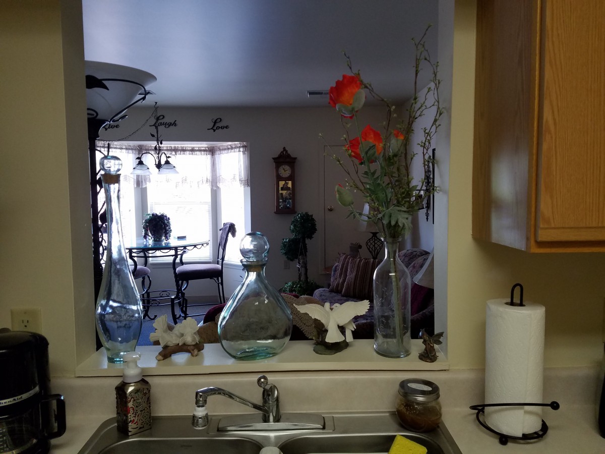 View from the kitchen sink, reflecting a dining area through the mirror with flowers and bottles on the counter.