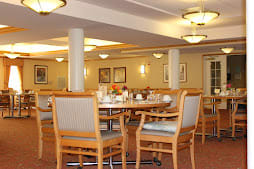 A cozy dining area with neatly arranged tables and chairs, softly lit by ceiling lights.