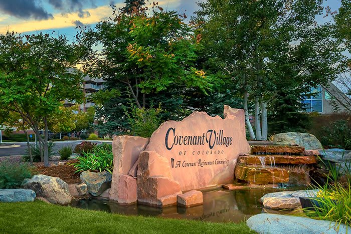 A scenic view of a stone sign for Governor's Village, surrounded by lush greenery and a water feature.