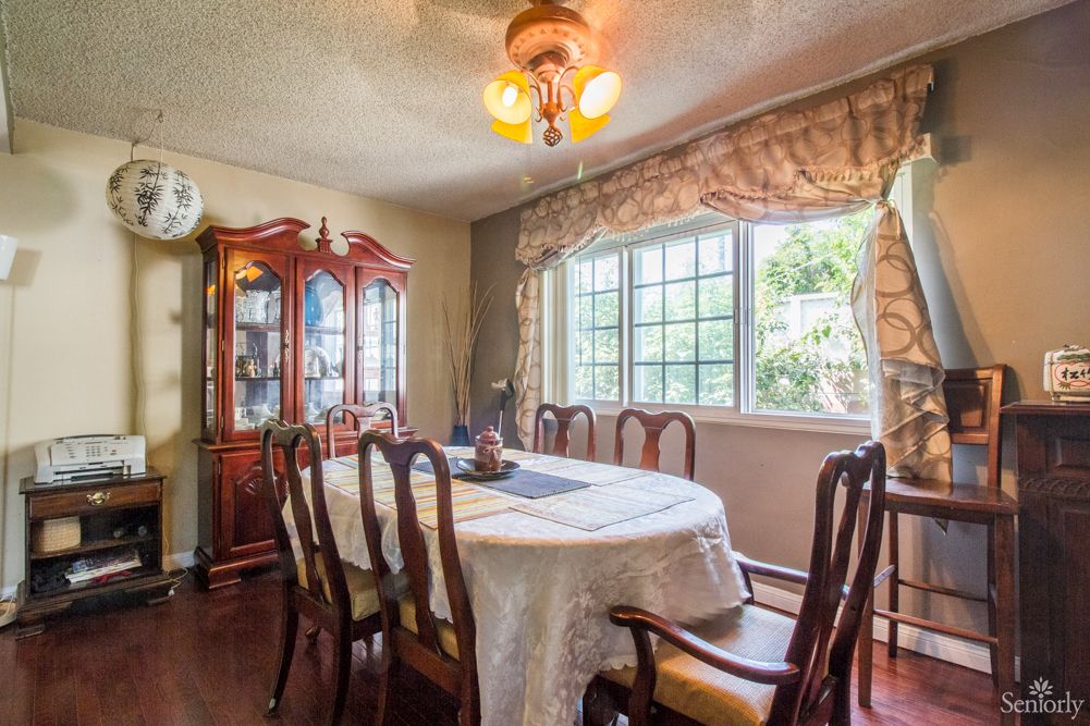 A well-lit dining room with a large table, chairs, and a china cabinet by the window.