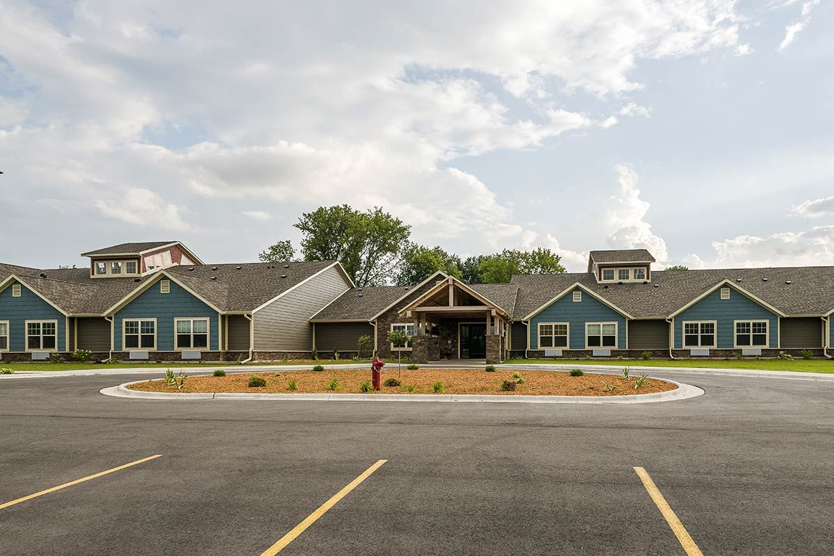 A modern residential building with a landscaped driveway under a partly cloudy sky.