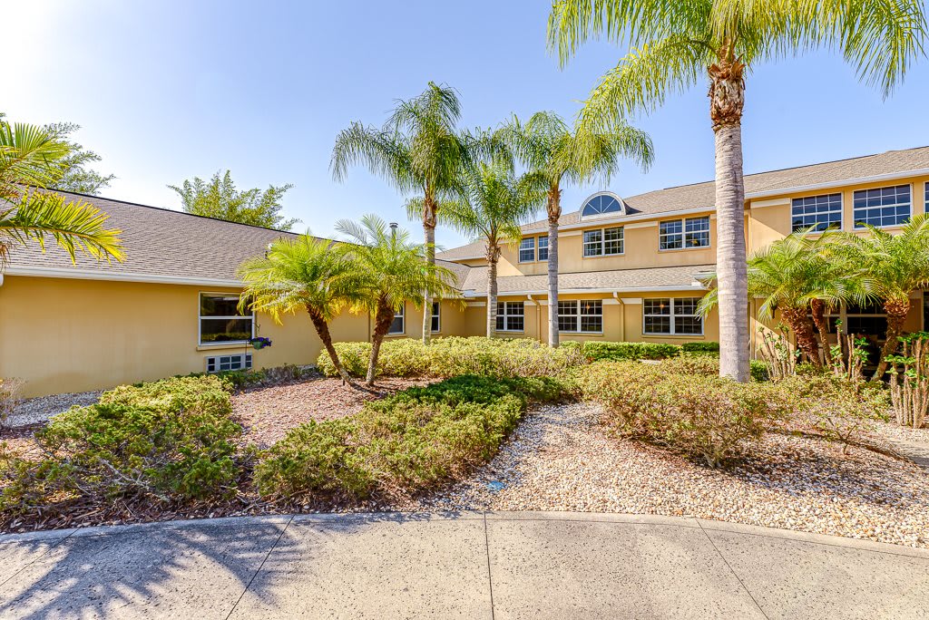 A two-story residential house with palm trees and landscaped surroundings on a sunny day.
