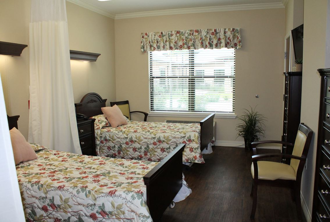 A cozy bedroom with two twin beds, floral bed covers, and a window letting in natural light.