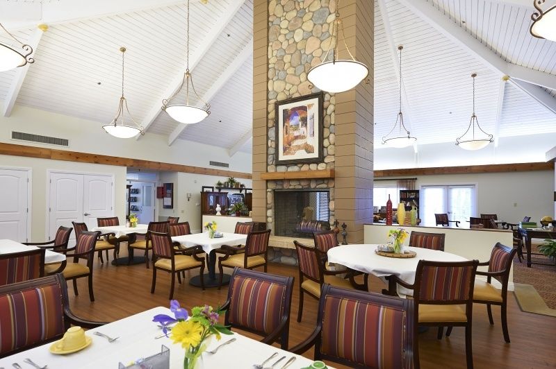 A spacious dining area with well-arranged tables and chairs, featuring a central fireplace and decorative lighting.