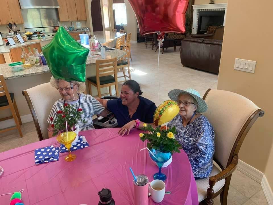 A group of people smiling at a table decorated with balloons and flowers indoors.