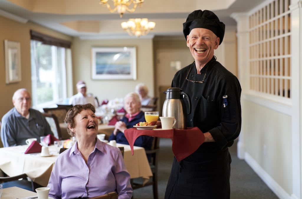 A cheerful server in a dining room bringing coffee to an elderly group, creating a warm and friendly atmosphere.