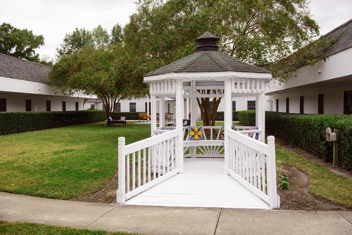 A white gazebo with a walkway in a peaceful park setting surrounded by trees and greenery.