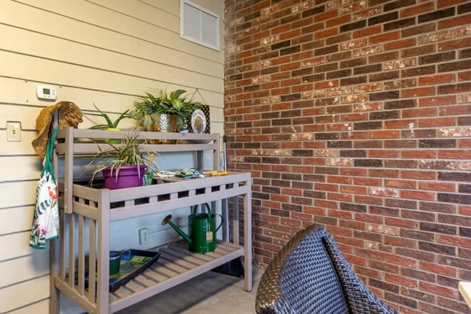 A cozy corner with a potting bench and potted plants against a brick wall.