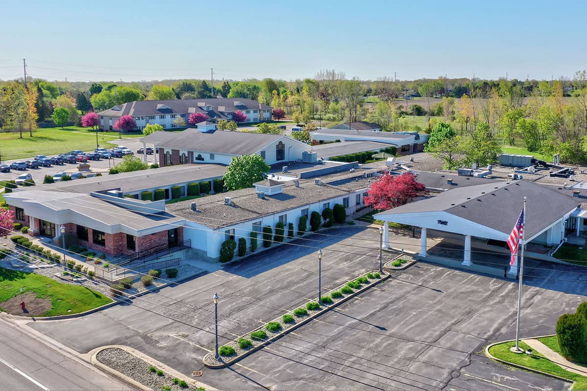 Aerial view of a suburban area featuring buildings, a parking lot, and lush green trees with blooming flowers.