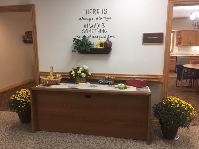 A decorative indoor setup featuring a motivational quote, flowers, and a fruit basket on a wooden console.