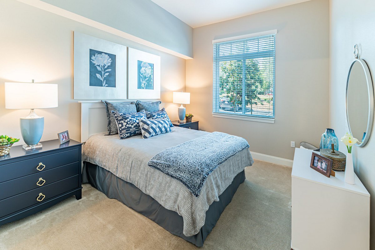 A cozy bedroom with modern decor, featuring a comfortable bed, two nightstands with lamps, and a large window providing natural light.