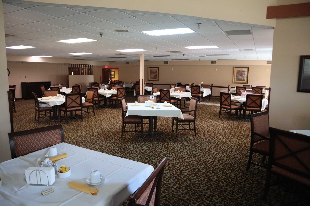 An empty dining room with set tables and chairs, featuring a carpeted floor.