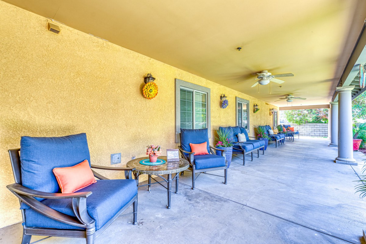 A cozy outdoor patio with blue cushioned chairs and small tables against a yellow wall.