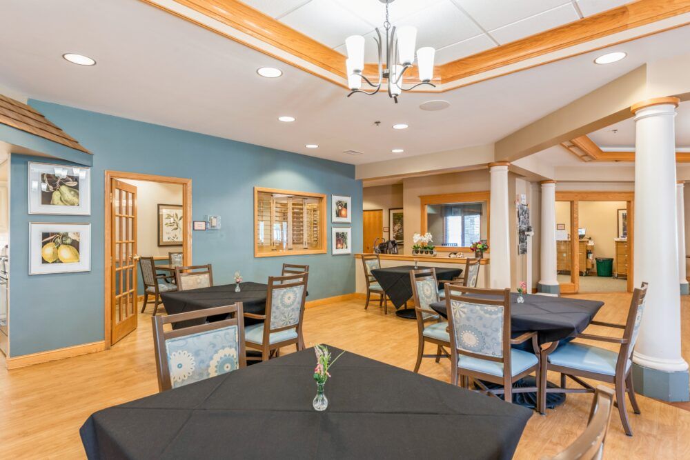 A cozy dining room with neatly arranged tables and chairs, featuring a chandelier and warm decor.
