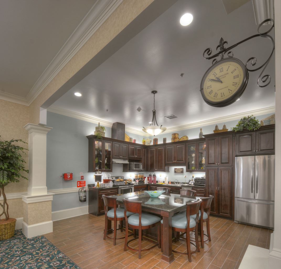 A modern kitchen and dining area featuring wood cabinets, a large clock, and stainless steel appliances.