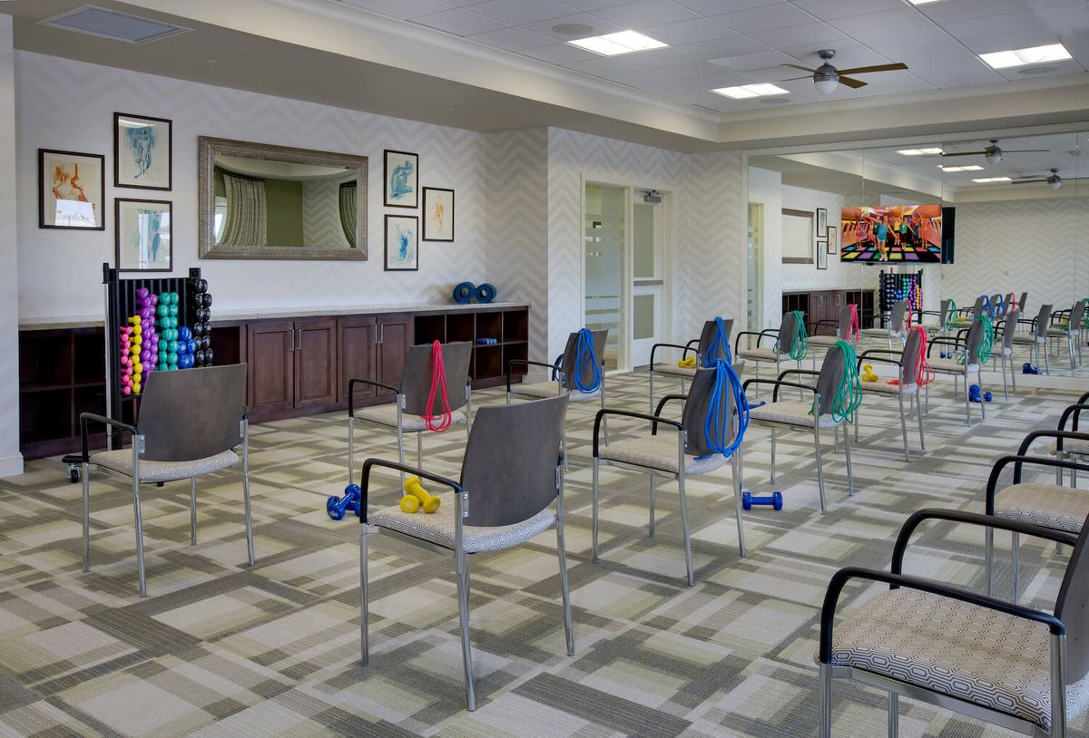 An exercise room with chairs set up for a fitness class, each equipped with a pair of dumbbells.