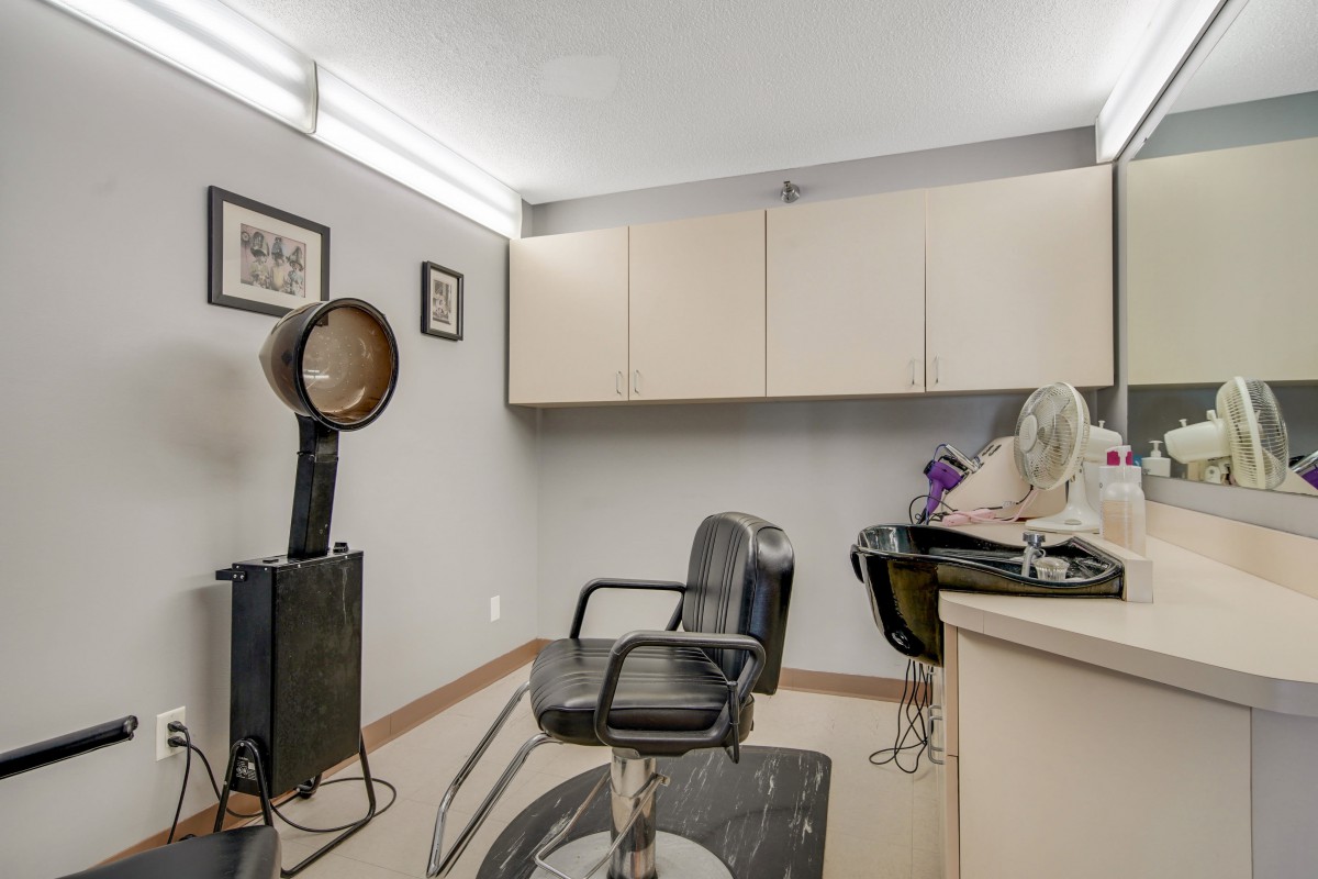A hair salon interior featuring a salon chair, hair dryer, and sink.