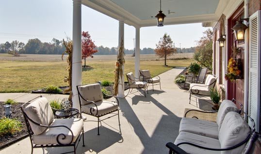 A cozy porch with comfortable seating overlooks a sunny garden landscape.
