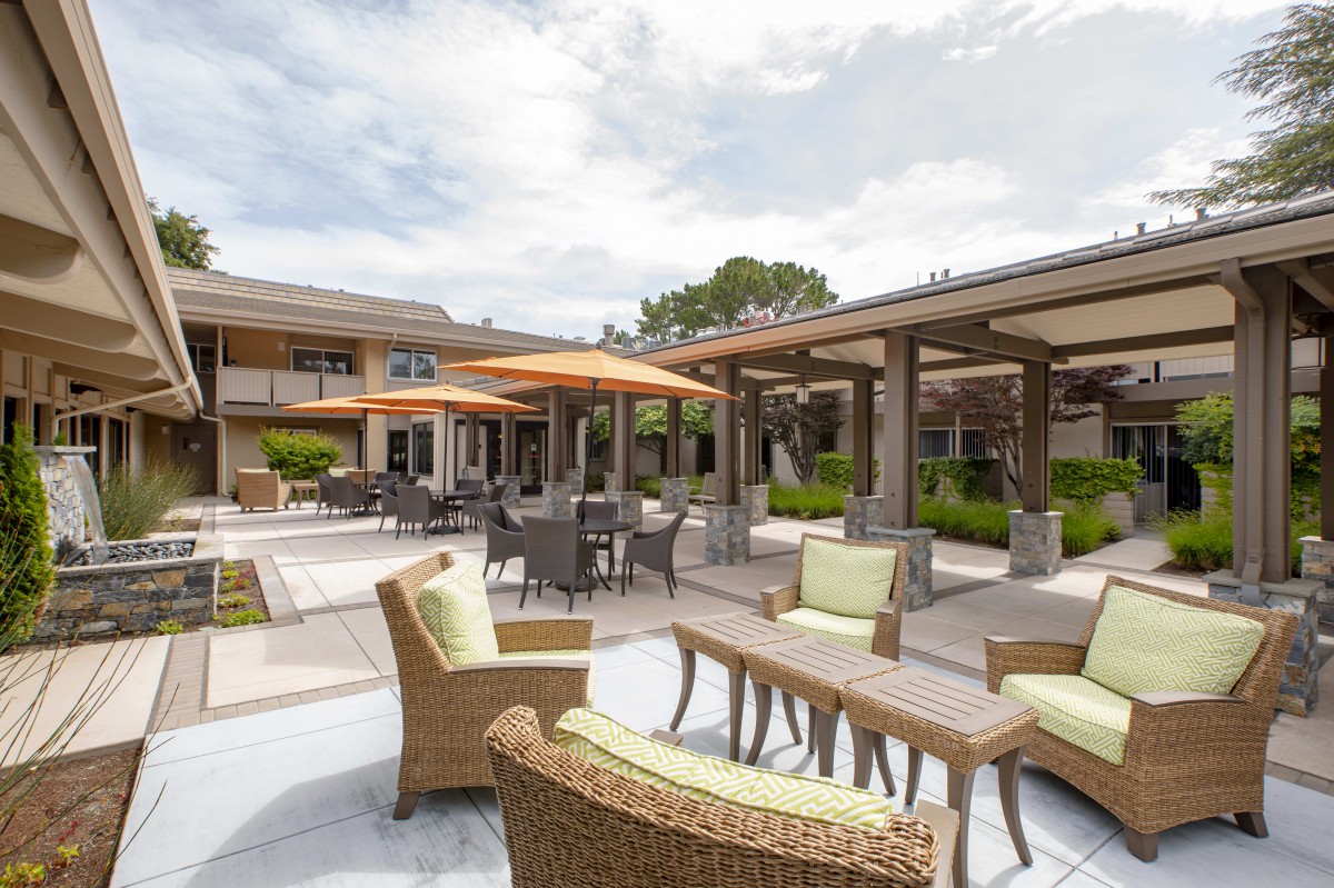 A spacious outdoor patio area with wicker furniture and large umbrellas, surrounded by a landscaped garden.