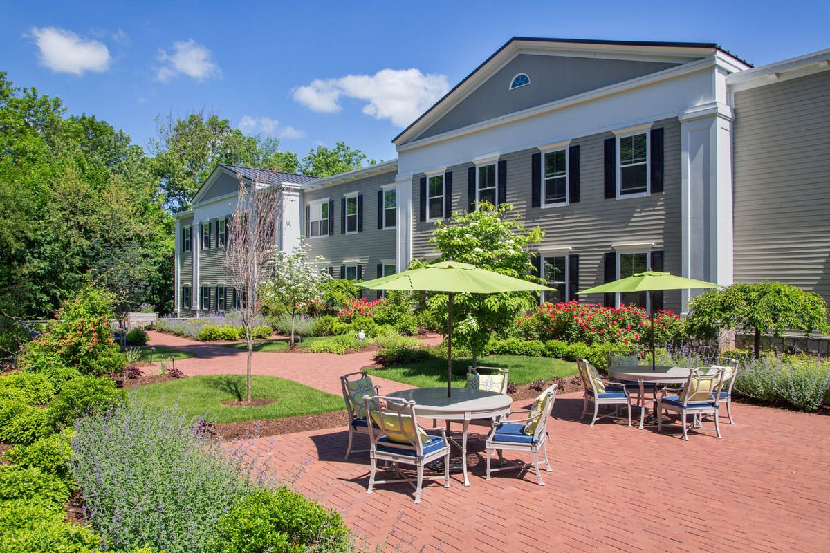 A peaceful outdoor patio area with seating and umbrellas in front of a large building on a sunny day.
