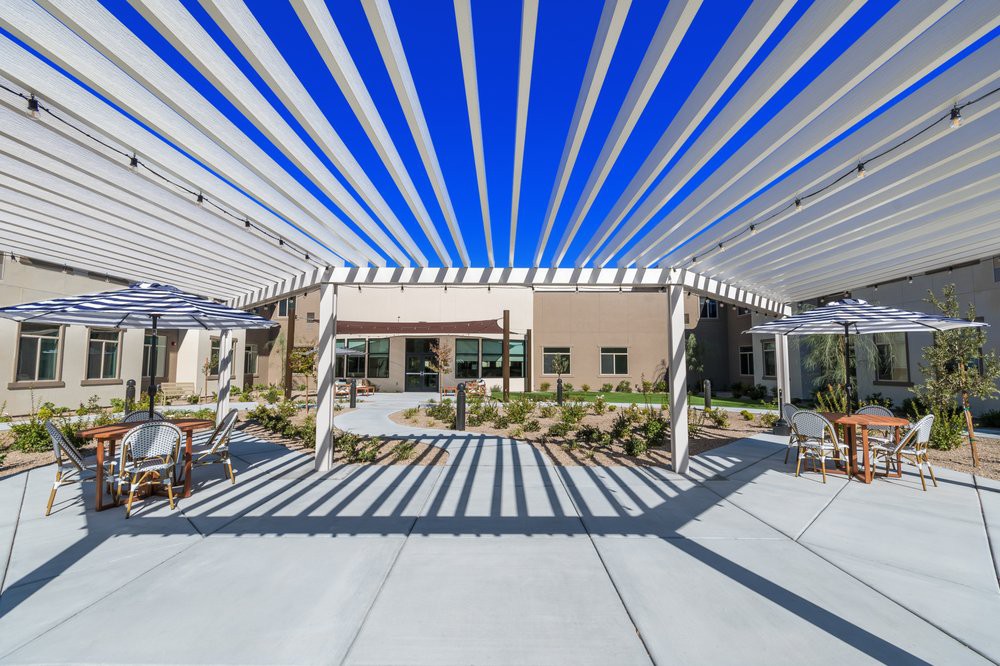 A modern patio area features a pergola casting striped shadows across the ground.
