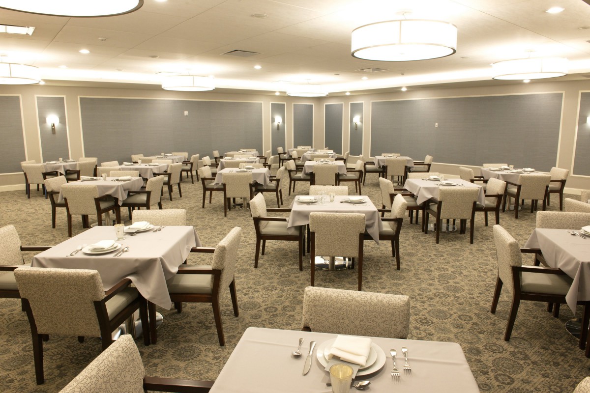 An elegant dining room with neatly arranged tables and chairs, featuring soft lighting and a spacious layout.