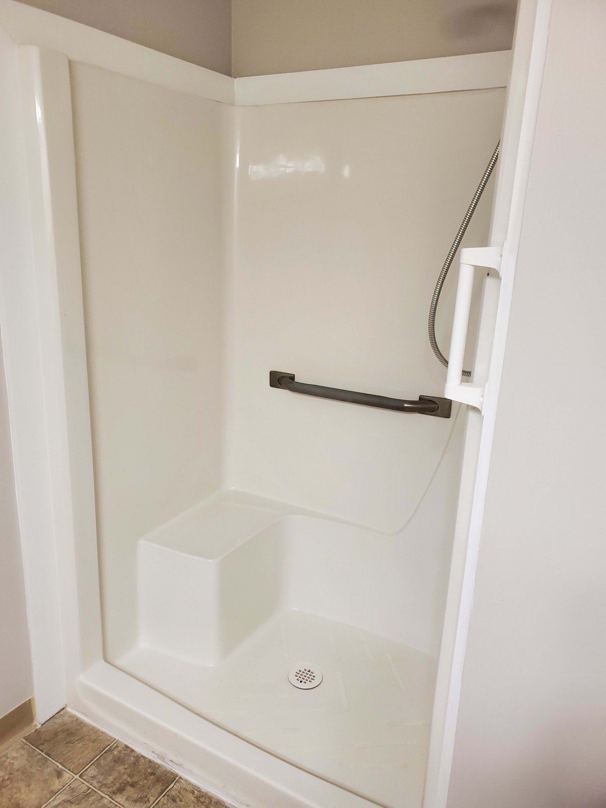 A modern, clean shower with a built-in seat and grab bar.