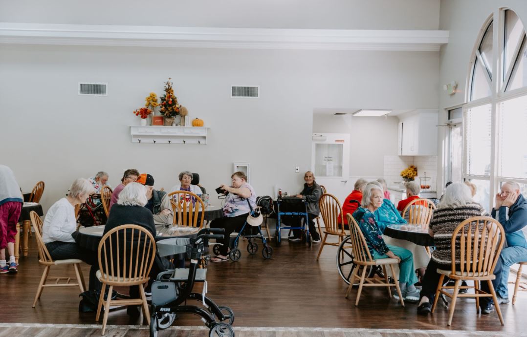 A group of elderly individuals seated and interacting in a communal indoor space.