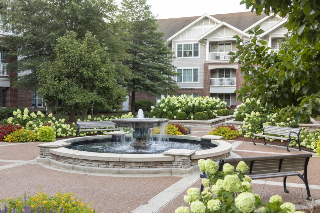 A beautifully landscaped garden featuring a central fountain with a residential building in the background.