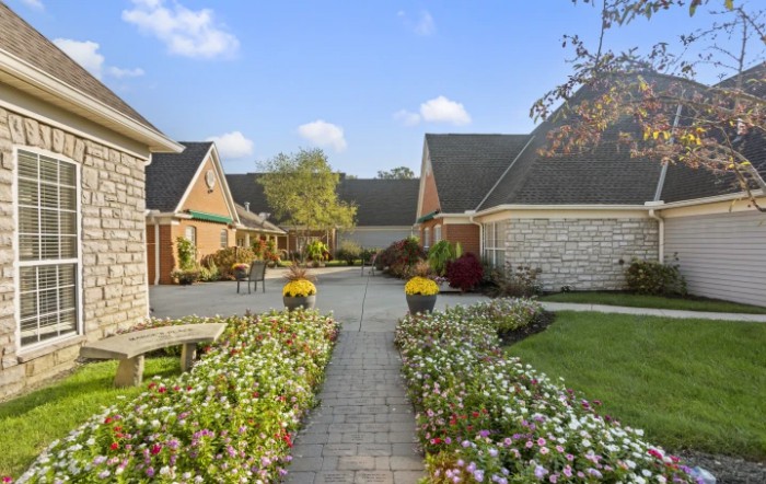A picturesque garden pathway surrounded by houses, adorned with vibrant flowers under a clear blue sky.