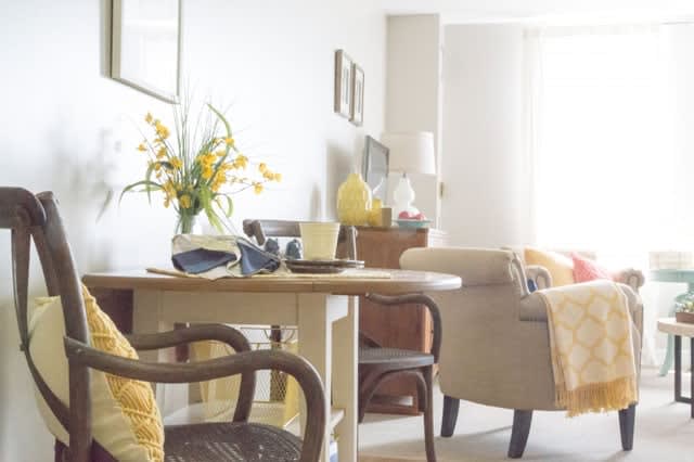 A bright and cozy living room with a wooden table, chairs, a sofa, and floral decorations.