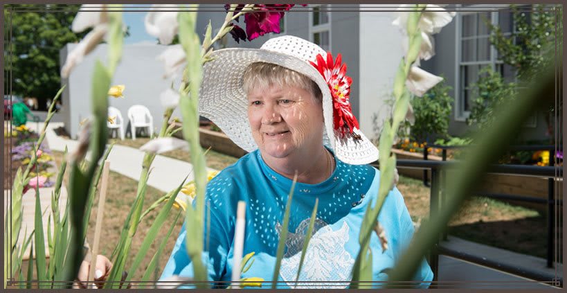 A woman wearing a hat with flowers, sitting outdoors in a garden.