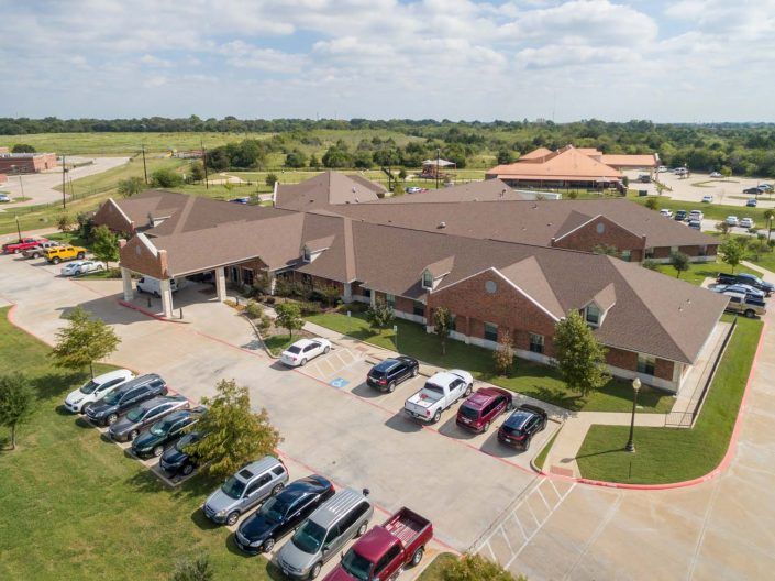 Aerial view of a suburban building with a parking lot filled with cars under a cloudy sky.