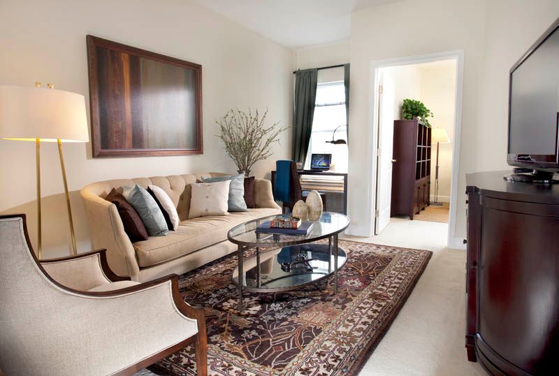 A cozy living room featuring a comfortable sofa, glass coffee table, and decorative rug with a window providing natural light.