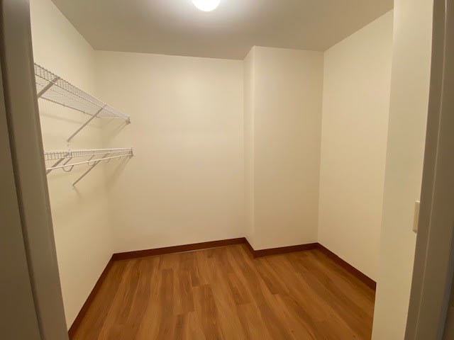 An empty closet with wooden flooring and white walls, featuring shelves on the side.