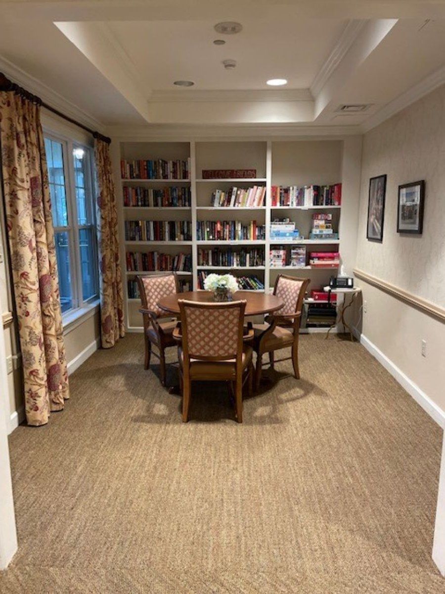 A cozy reading room with a round table and chairs, surrounded by bookshelves.