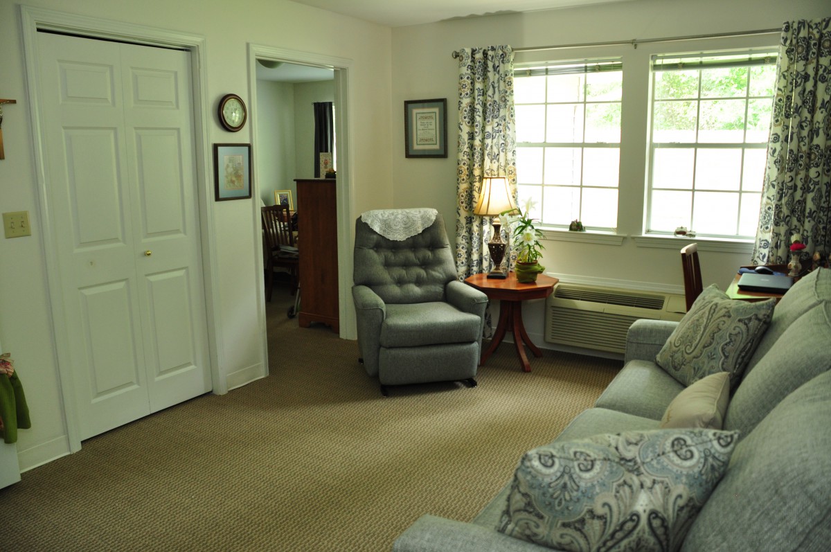 A cozy living room with an armchair, sofa, and a lamp next to the window.