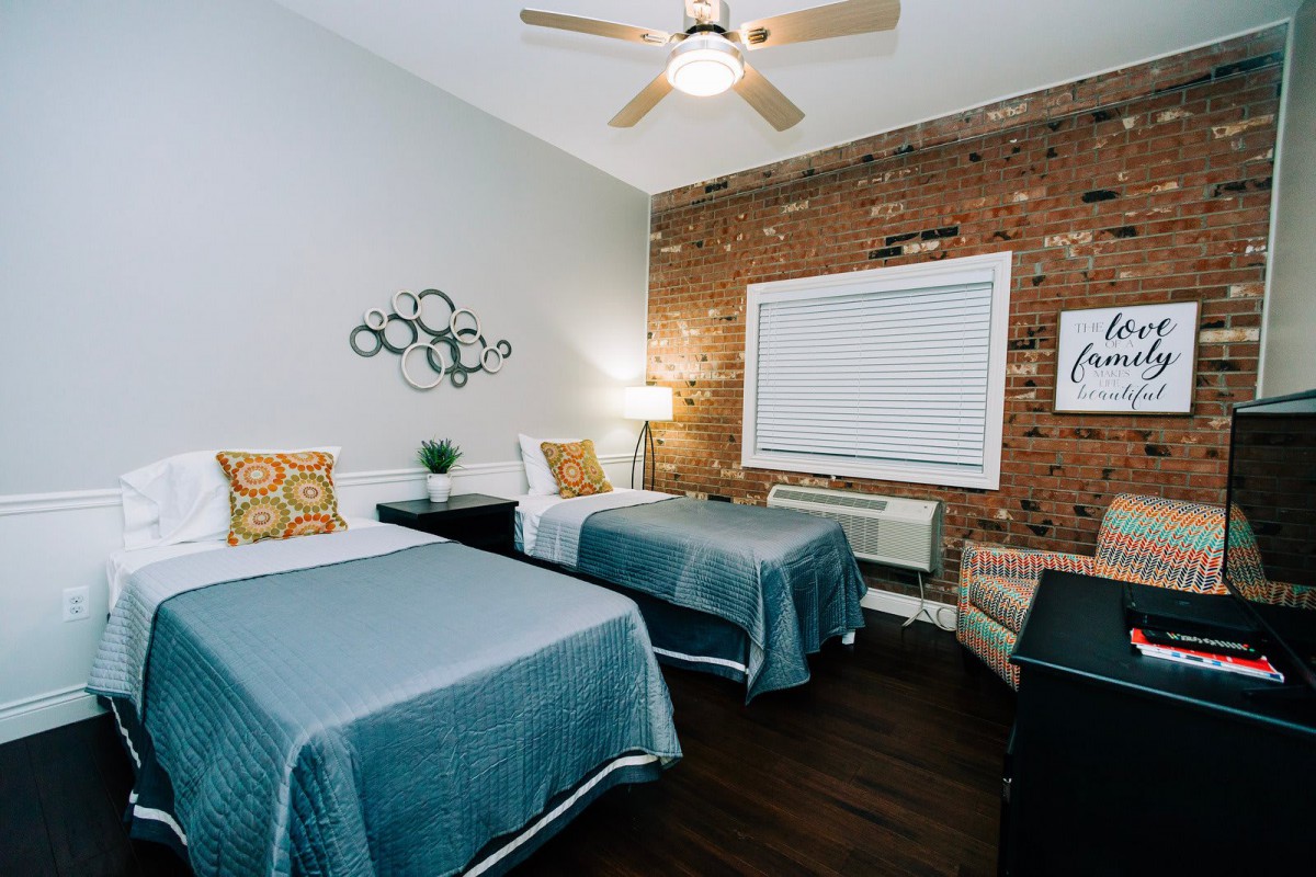 A cozy bedroom with twin beds, featuring a brick accent wall and modern decor.