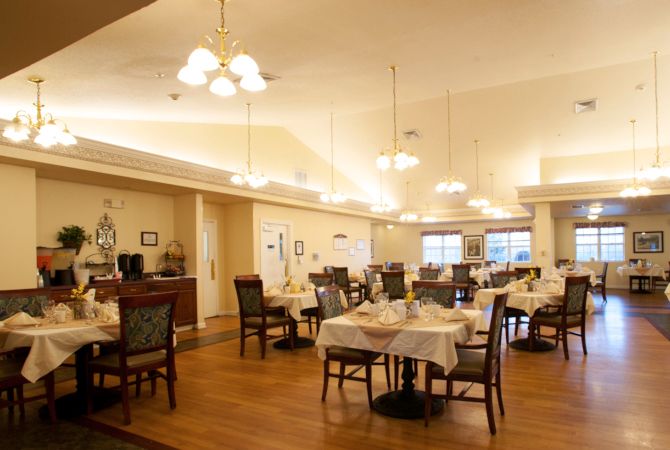 A cozy restaurant dining area with neatly arranged tables and chairs, warmly lit by overhead lights.